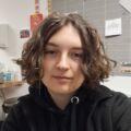 Face of a woman with curly short brown hair, staring at the camera